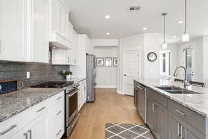 Kitchen featuring stainless steel appliances, light stone countertops, two tone cabinets, light wood-type flooring, and hanging light fixtures