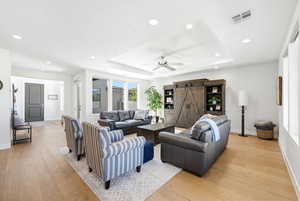 Living area with light wood-type flooring, a barn door, recessed lighting, a ceiling fan, and a raised ceiling
