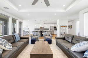 Living room with light wood finished floors, a raised ceiling, recessed lighting, and a ceiling fan