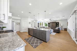 Kitchen with light stone counters, light wood finished floors, open floor plan, a kitchen island with sink, and a tray ceiling