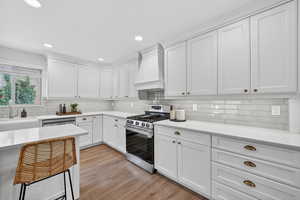Kitchen with stainless steel appliances, white cabinets, light wood-style flooring, recessed lighting, and light stone countertops