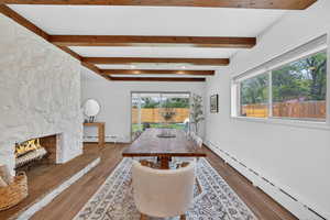 Dining area featuring baseboard heating, a stone fireplace, wood finished floors, recessed lighting, and beamed ceiling