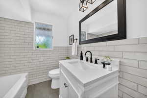 Full bath with vanity, a wainscoted wall, a tub to relax in, and tile walls