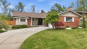 Ranch-style house with board and batten siding, concrete driveway, a front yard, and brick siding
