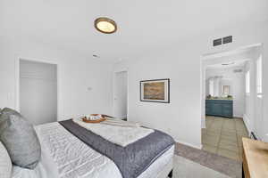 Bedroom featuring light tile patterned floors, a closet, light carpet, a baseboard radiator, and ensuite bath