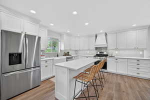 Kitchen with stainless steel appliances, white cabinetry, a kitchen breakfast bar, light wood-style flooring, and recessed lighting