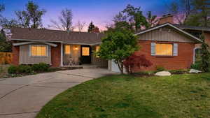 Ranch-style home with board and batten siding, a chimney, concrete driveway, brick siding, and a front yard