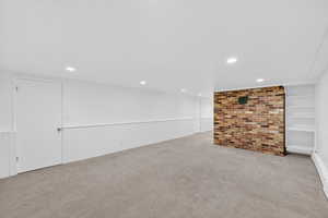 Finished below grade area featuring light carpet, built in shelves, a wainscoted wall, recessed lighting, and brick wall