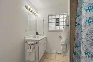 Full bathroom featuring vanity, a shower with shower curtain, light tile patterned floors, and a textured ceiling
