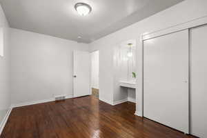Unfurnished bedroom with dark wood-type flooring, built in desk, and a closet