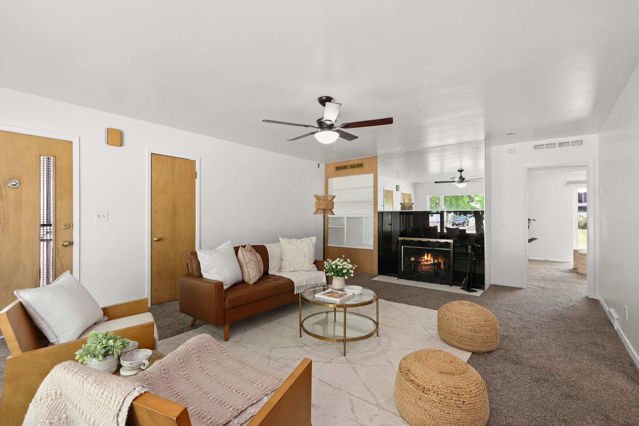 Carpeted living area featuring a fireplace with a black surround, a ceiling fan, and light wood-finish doors