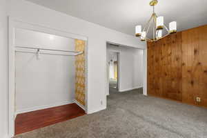 Unfurnished bedroom featuring dark carpet, a chandelier, and wooden walls