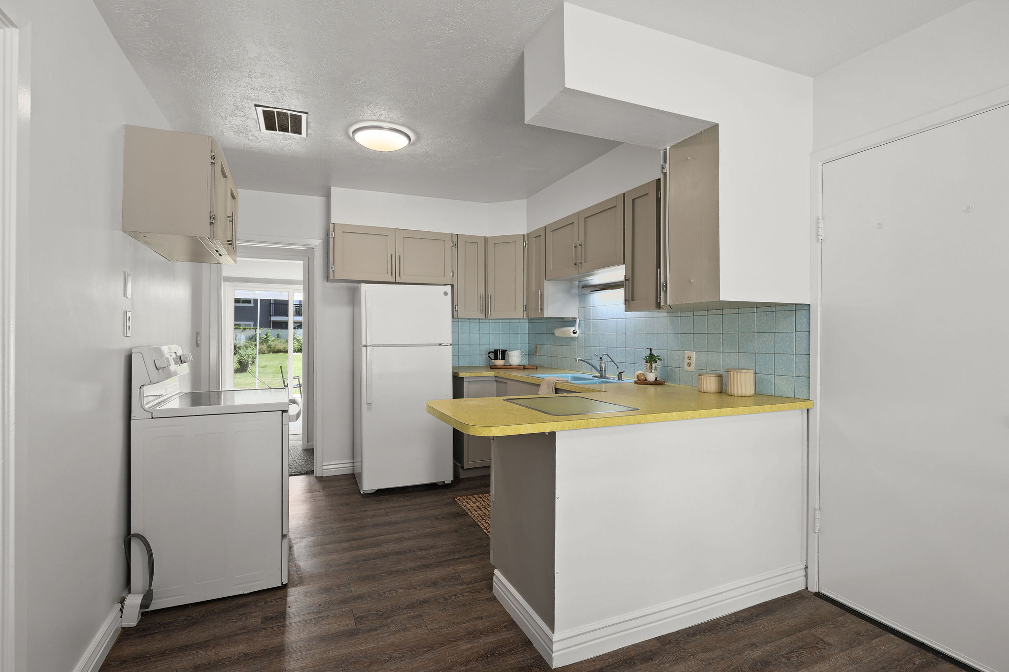 Kitchen featuring wood-finish flooring, a vibrant blue tile backsplash, light gray cabinetry, and a bright yellow countertop