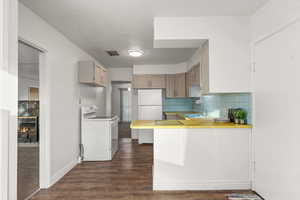 Kitchen featuring white appliances, light countertops, a peninsula, a lit fireplace, and dark wood-type flooring