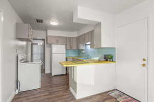 Kitchen featuring white appliances, light countertops, a peninsula, backsplash, and dark wood-type flooring