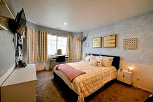 Bedroom with wallpapered walls, an office area, a wainscoted wall, and dark colored carpet