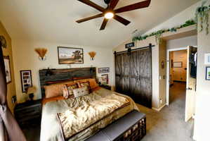 Bedroom featuring a barn door, vaulted ceiling, a closet, carpet floors, and ceiling fan