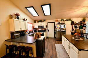 Kitchen with stainless steel appliances, a breakfast bar area, white cabinetry, vaulted ceiling, and a peninsula