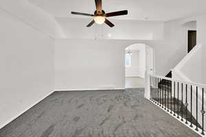 Empty room featuring arched walkways, a ceiling fan, lofted ceiling, and carpet
