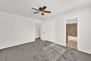 Unfurnished bedroom with dark carpet, a ceiling fan, connected bathroom, a closet, and dark tile patterned flooring