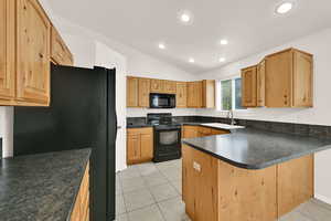 Kitchen with black appliances, dark countertops, vaulted ceiling, light tile patterned floors, and a peninsula