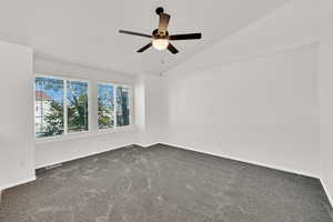 Empty room with dark carpet, vaulted ceiling, and ceiling fan