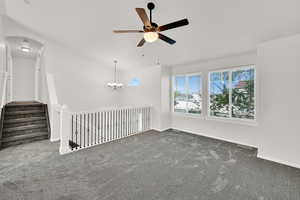 Empty room featuring dark colored carpet, a ceiling fan, hanging lights, arched walkways, and vaulted ceiling