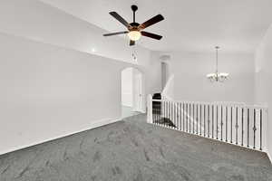 Empty room featuring carpet floors, a ceiling fan, lofted ceiling, hanging lights, and arched walkways