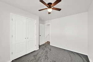 Unfurnished bedroom with dark colored carpet, a closet, and a ceiling fan