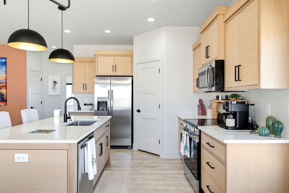 Kitchen featuring light wood finish cabinets, a center island with sink, stainless steel appliances, pendant lighting, and light wood-style flooring