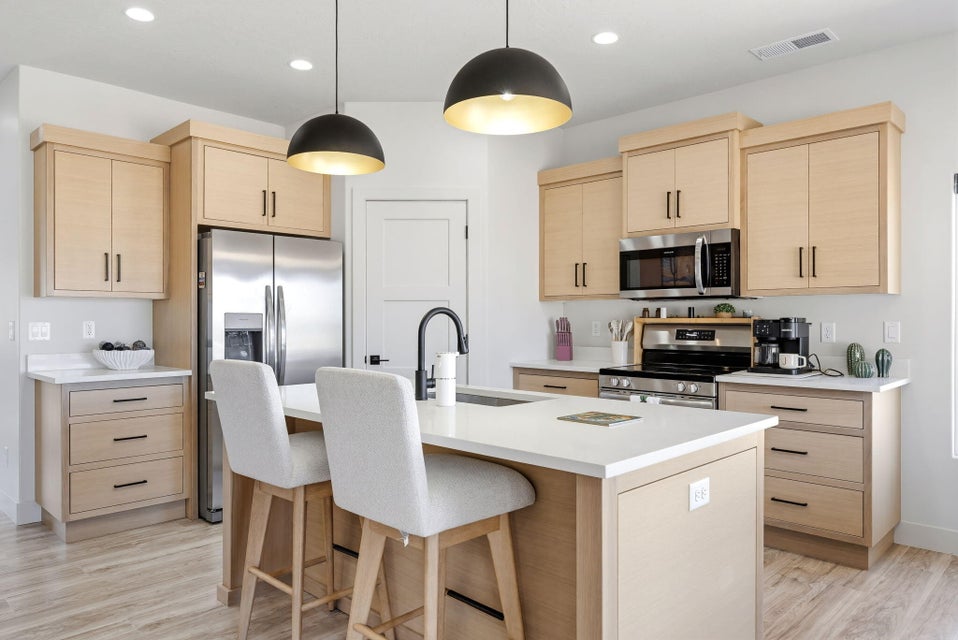Kitchen featuring light wood finish cabinetry, stainless steel appliances, an island with sink, a breakfast bar area, and pendant lighting
