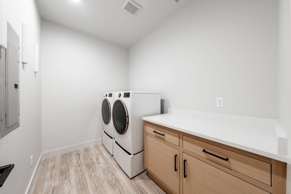 Laundry room featuring light wood-type flooring, washer and dryer, electric panel, and cabinet space