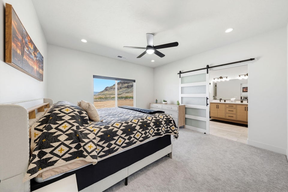 Bedroom with a barn door, ceiling fan, light carpet, recessed lighting, and ensuite bathroom