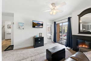 Living room with light tile patterned floors, light colored carpet, ceiling fan, and a glass covered fireplace