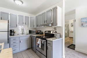 Kitchen with gray cabinets, stainless steel appliances, light stone countertops, and decorative backsplash