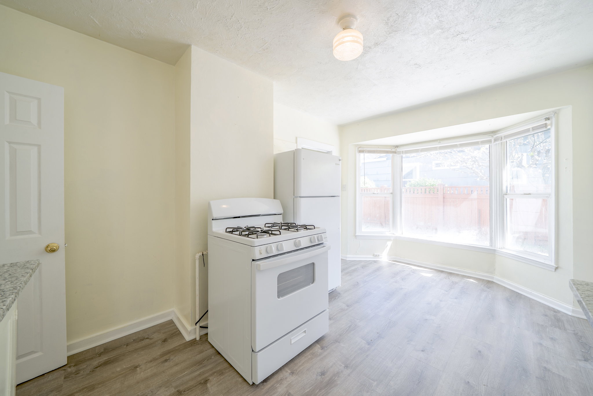 Kitchen with white appliances, light wood-style floors, a textured ceiling, white cabinets, and light countertops