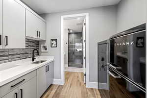 Kitchen featuring light wood-style floors, gray cabinetry, light stone countertops, and decorative backsplash