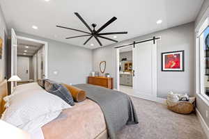 Bedroom with a barn door, light carpet, ceiling fan, recessed lighting, and connected bathroom
