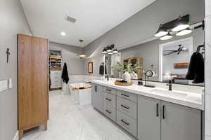 Bathroom with ensuite bathroom, double vanity, a spacious closet, light marble finish flooring, and a tub to relax in