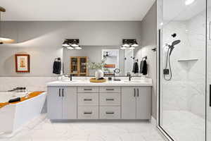 Full bathroom featuring double vanity, a freestanding tub, a marble finish shower, and light marble finish floors
