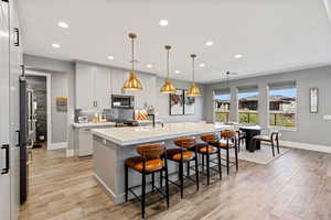 Kitchen with a kitchen breakfast bar, light wood-style flooring, pendant lighting, an island with sink, and tasteful backsplash