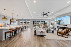 Living area featuring a tray ceiling, ceiling fan, light wood-style floors, plenty of natural light, and recessed lighting