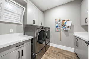 Laundry room featuring light wood-style floors, cabinet space, and washing machine and clothes dryer