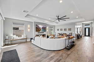 Living area with light wood finished floors, ceiling fan, recessed lighting, a raised ceiling, and a glass covered fireplace