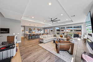 Living room with a tray ceiling, light wood-style flooring, recessed lighting, and a ceiling fan
