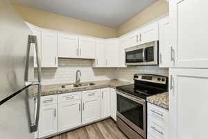 Kitchen with stainless steel appliances, white cabinets, light wood-type flooring, light stone countertops, and tasteful backsplash