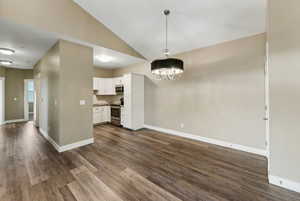 Unfurnished dining area with lofted ceiling, dark wood-type flooring, and suspended lighting