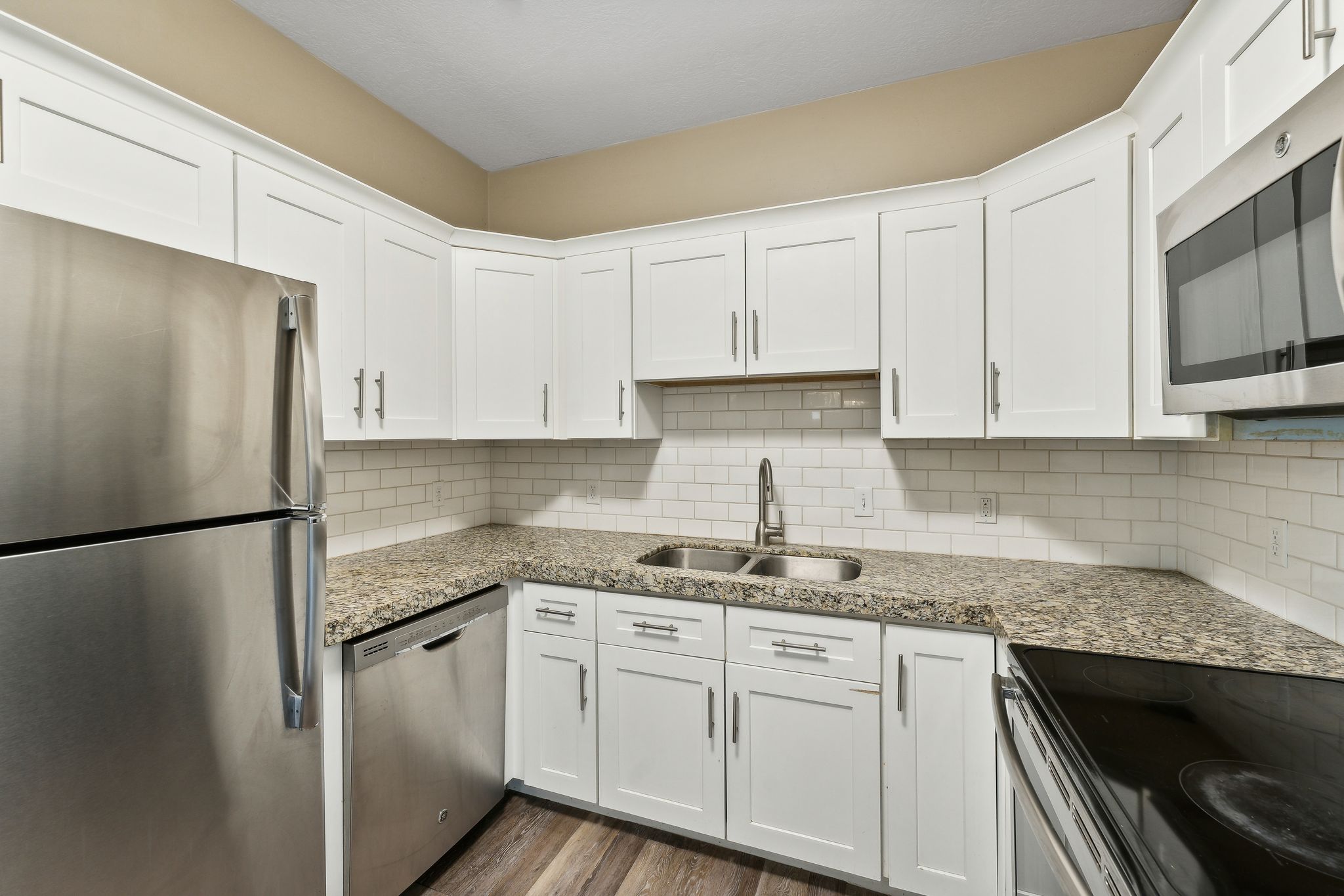 Kitchen featuring stainless steel appliances, white cabinets, light stone countertops, and dark wood-type flooring