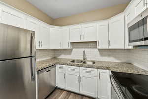Kitchen featuring stainless steel appliances, white cabinets, light stone countertops, and dark wood-type flooring