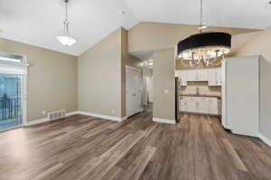 Kitchen with suspended lighting, white cabinetry, vaulted ceiling, dark wood-style floors, and backsplash